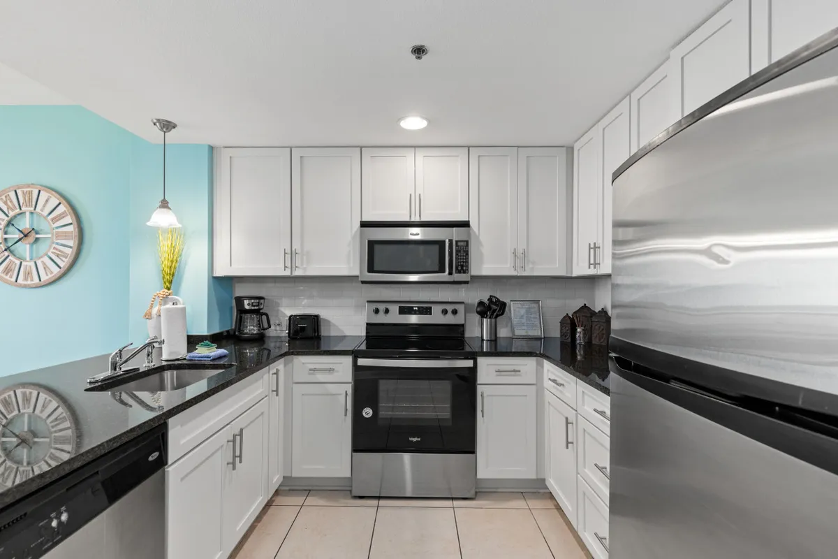A stylish modern kitchen featuring stainless steel appliances, black granite countertops, and light-colored cabinetry. The space is illuminated by a pendant light fixture above, and the kitchen is clearly equipped for both cooking and entertaining, with plenty of room for preparing meals and gathering.