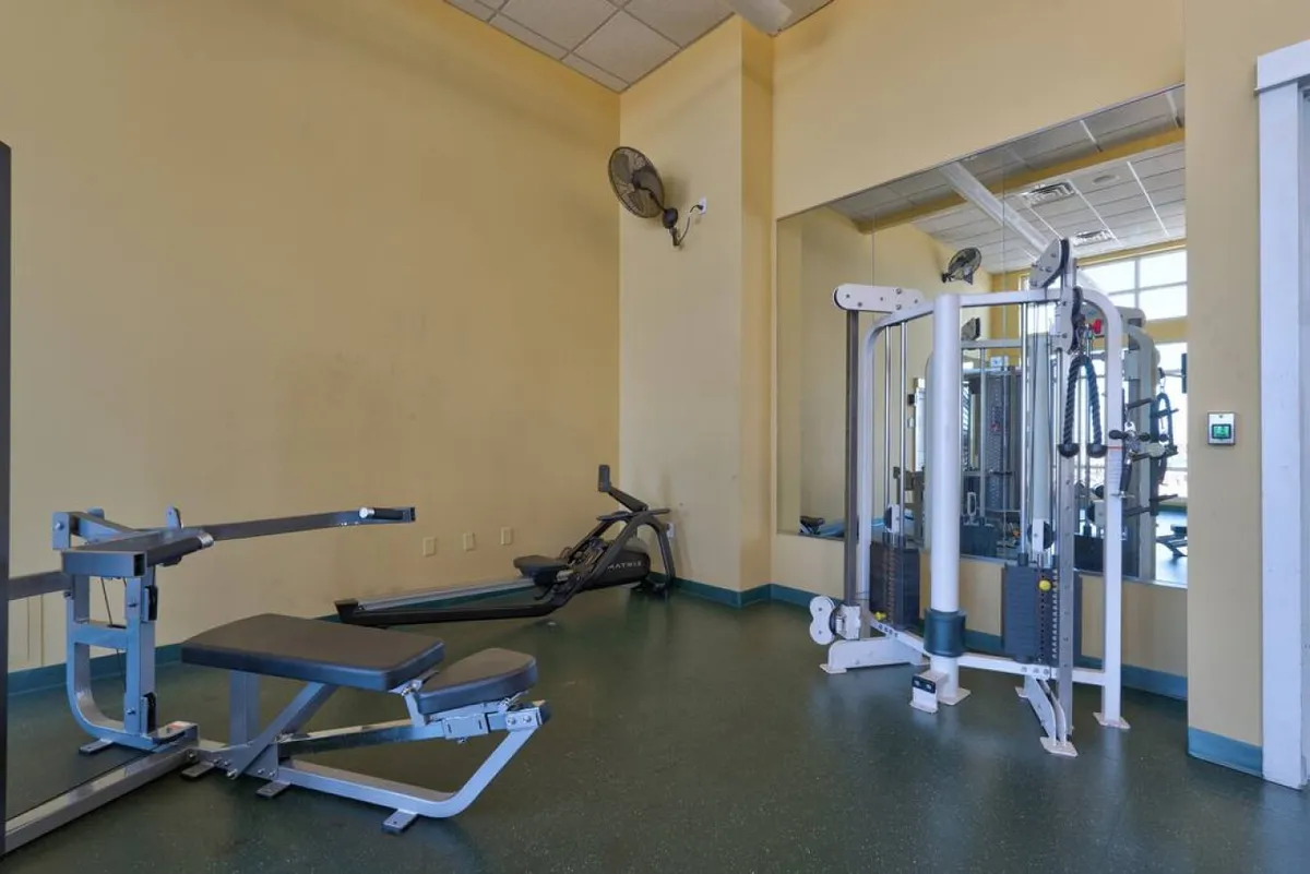 A well-equipped fitness center featuring modern exercise machines, mirrors, and an exercise mat. The atmosphere is energizing, ideal for morning workouts or active breaks during a remote workday.