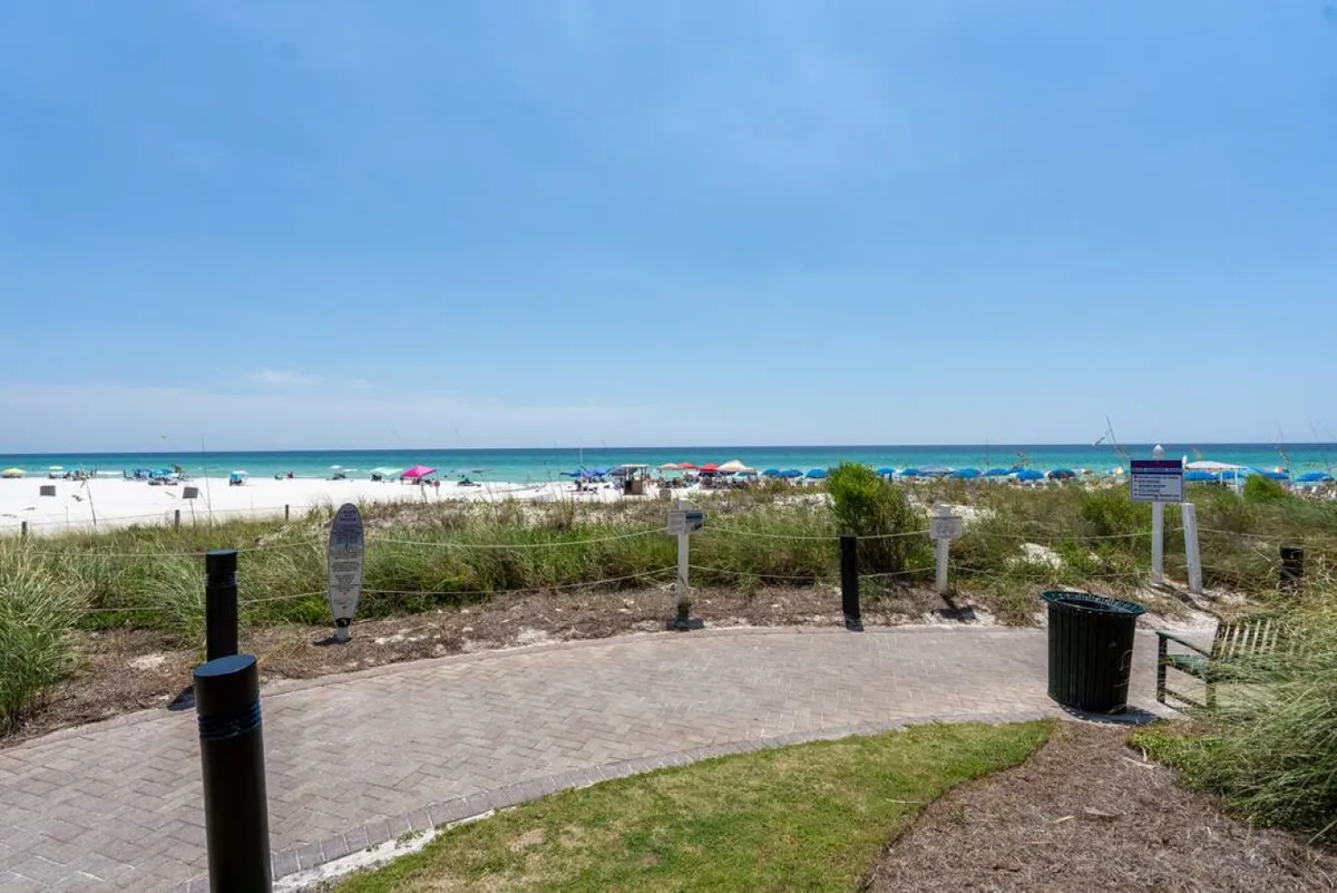 A welcoming exterior scene of the beach and ocean, dotted with chairs and umbrellas, with a clear pathway leading to the shore. The environment is sunny and inviting, ideal for picnics, sunbathing, and leisurely walks.