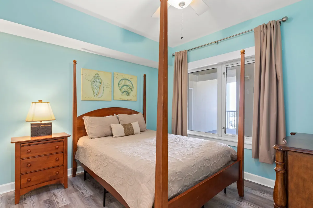 A serene king bedroom featuring a stylish four-poster bed with light-colored bedding, complemented by tasteful wall art and a nightstand with a lamp. Natural light filters in, creating a tranquil atmosphere ideal for restful nights.