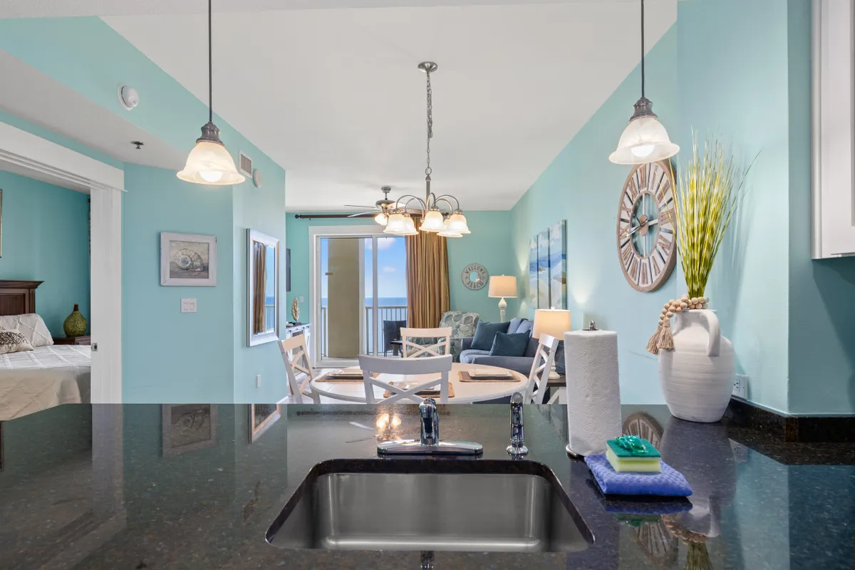 This image captures the kitchen sink and countertop area, a dining table with chairs, a living room seating area, and a balcony with an ocean view. The open-plan layout connects the kitchen and dining space to social and relaxation areas, embodying the communal spirit described in the section.