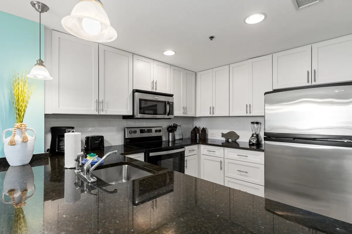 This image features a modern kitchen with black granite countertops, stainless steel appliances, white cabinetry, and a kitchen sink with faucet. The inviting atmosphere suggests a space ready for cooking, preparing coffee, and sharing casual snacks, with ample room for meal preparation and cleanup.