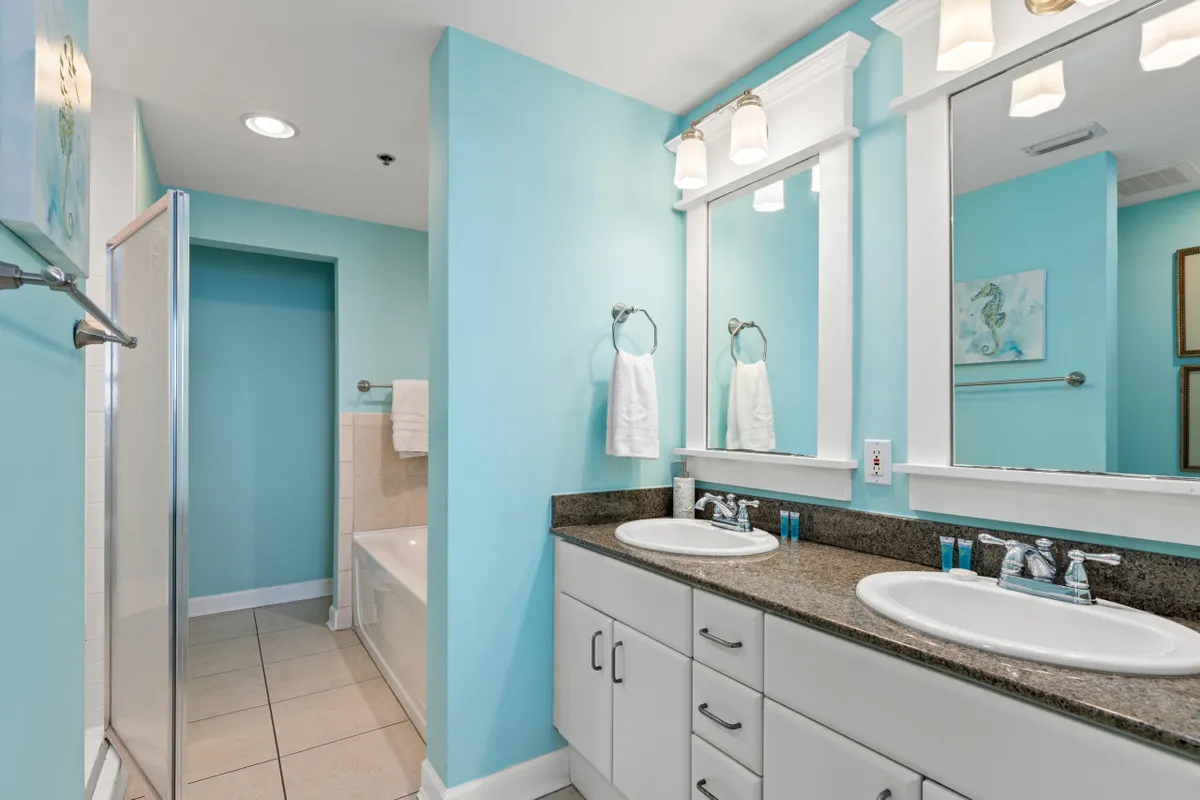 A spacious, modern bathroom featuring a double sink vanity with granite countertop, large mirrors, a bathtub with a tiled surround, and a glass-enclosed shower. The space is bright, clean, and designed for convenience and relaxation.
