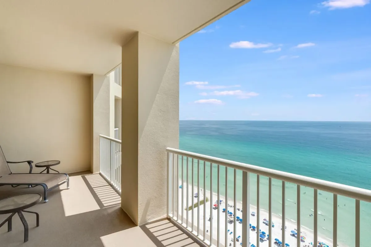 A private balcony setup with comfortable seating, offering a sweeping panoramic view of the Gulf of Mexico and the white sandy beach below. The atmosphere is tranquil, providing a space to relax and enjoy the sea breeze.