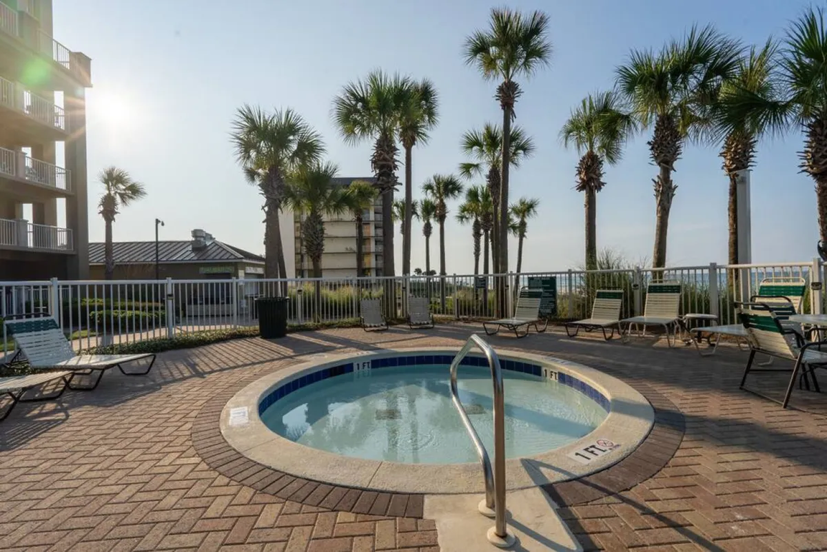 A circular heated spa/hot tub is surrounded by palm trees and lounge chairs, all enclosed within a secure fenced area. The setting feels private yet open to the tropical outdoors, perfect for unwinding after a day on the beach.