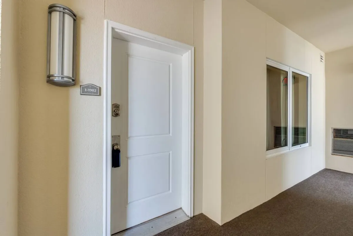 A welcoming entrance view of the condo, featuring a clean white door with a unit plaque, modern lighting, and a window letting in natural light. This image provides a sense of arrival and anticipation, marking the transition from outside adventures to resort comfort.